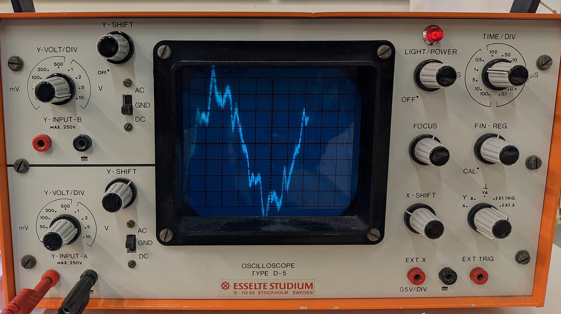 Analog oscilloscope tube displaying a harmonic waveform trace